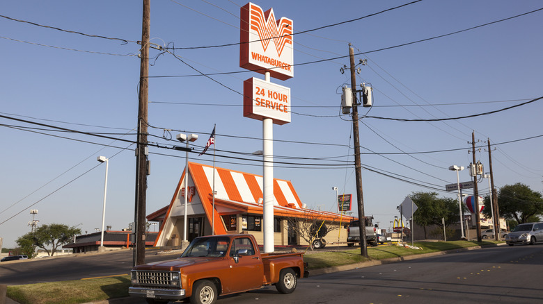 Cars park outside of a Whataburger, with a brown vintage pickup truck in the foreground.