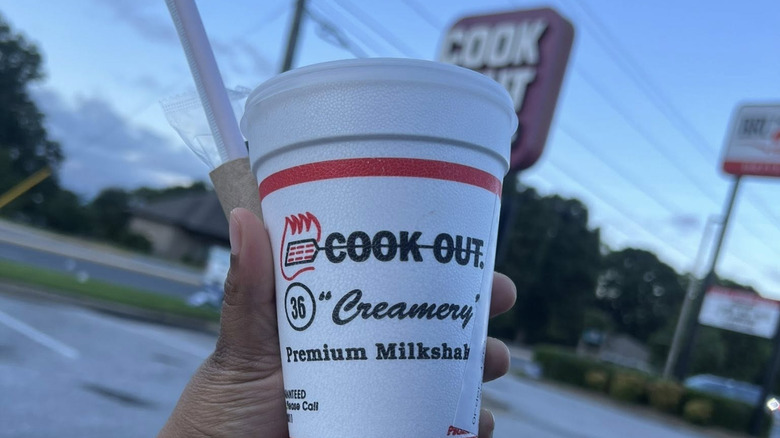 person holding Cook Out milkshake with restaurant parking lot sign in background