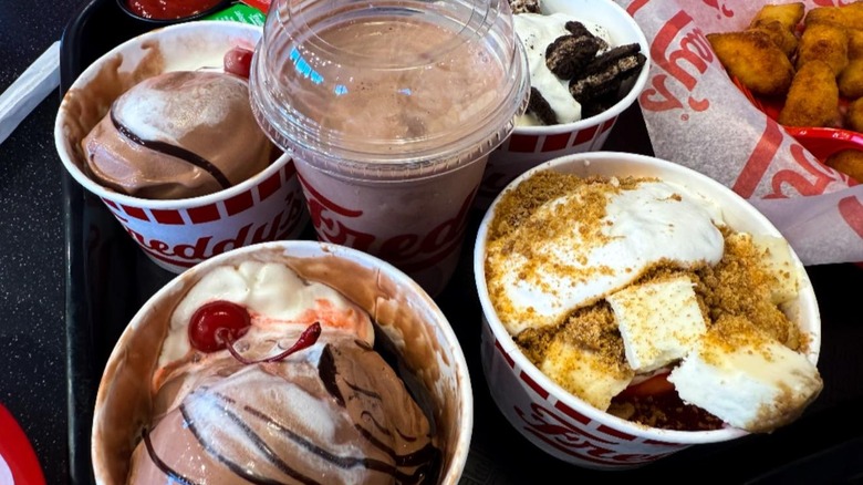 tray full of Freddy's frozen custard in cups with various toppings and chocolate milkshake