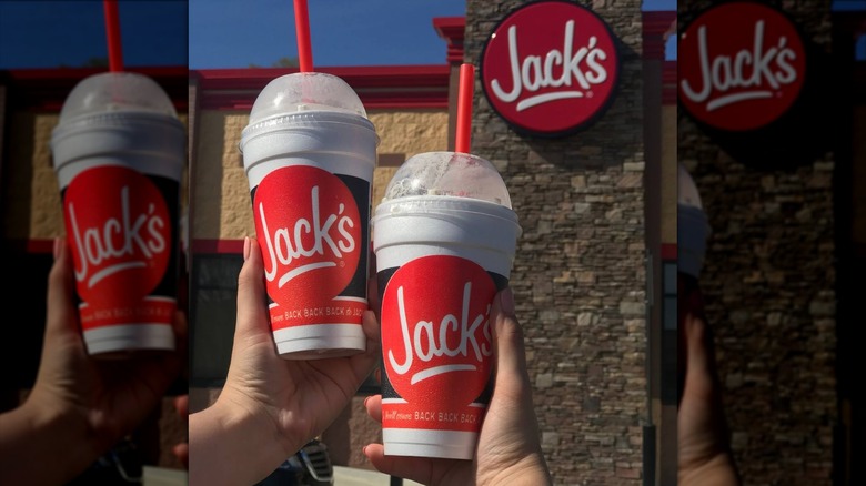 Two hands hold Jack's milkshakes in to-go cups in front of Jack's location
