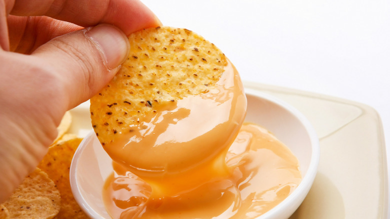 hand dipping tortilla chip into cheese sauce