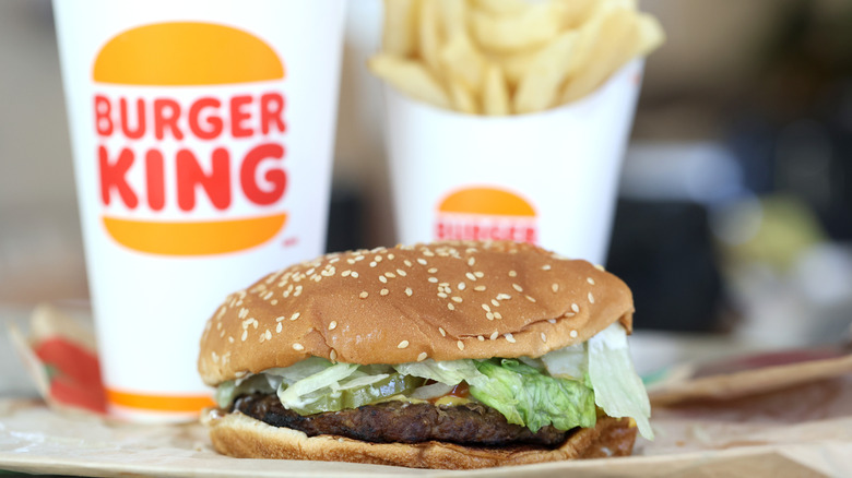 Whopper with Burger King logo drink and fries in background.