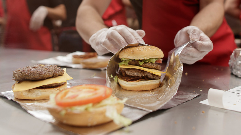 Hands of employee wrapping double cheeseburgers in foil.