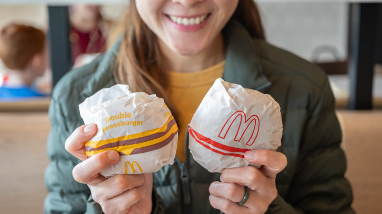 View of woman, with focus on hands holding two wrapped McDonald's burgers in logo wrappers.