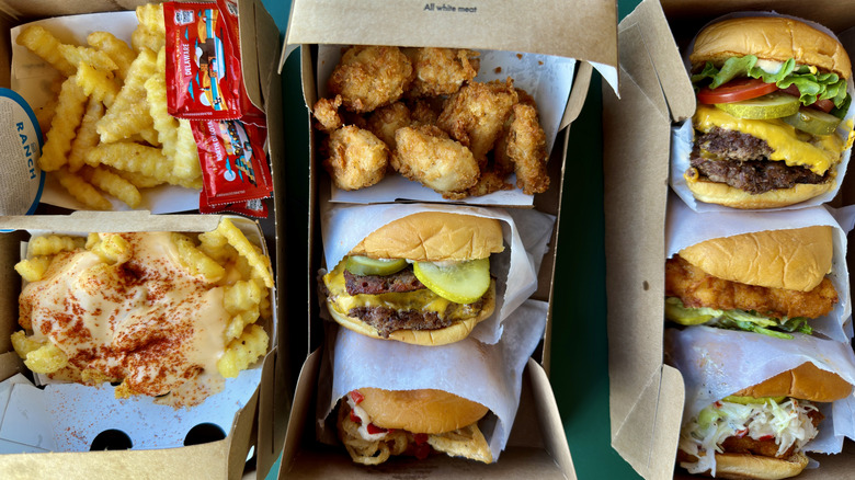 Shake Shack spread including wings, burgers, sandwiches, and crinkle cut fries, with sauce packets.