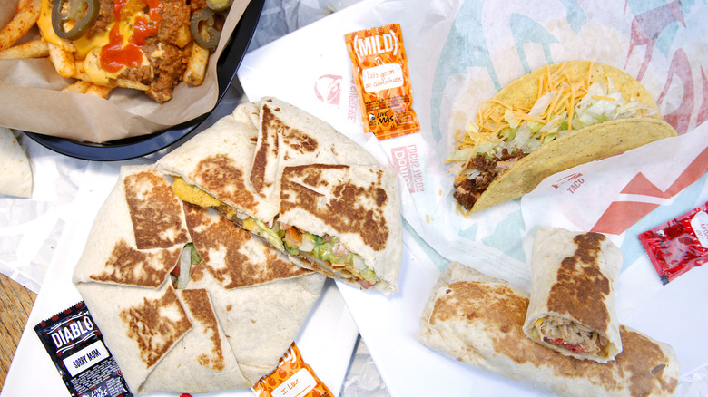 Taco Bell taco, fries, Crunchwrap and burrito, sitting on wrappers with various sauce packets.