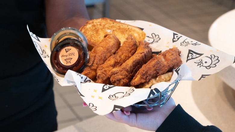 Hand holding a tray of PDQ Chicken tenders with two sauces