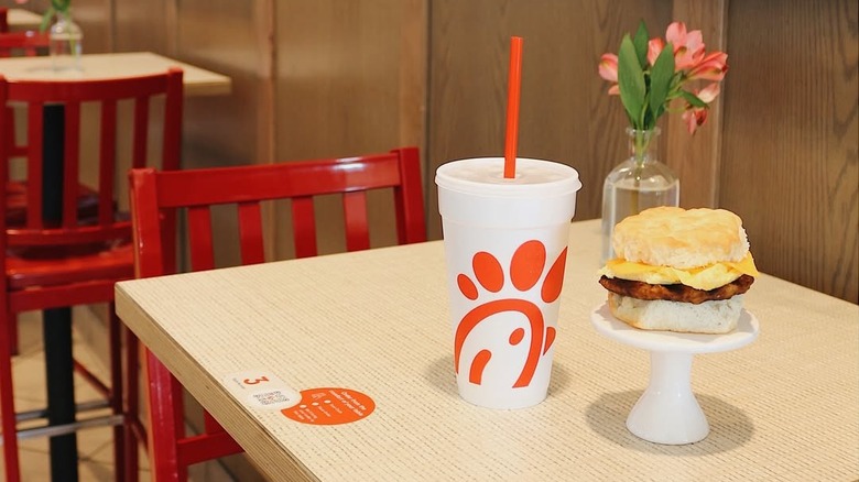 Sausage egg and cheese biscuit on a small white pedestal with a soda sitting on the countertop of a table from Chick-fil-A