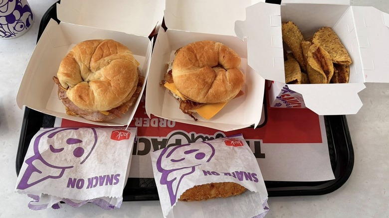 Jack in the box breakfast sandwiches and tacos in to-go containers on a plastic tray