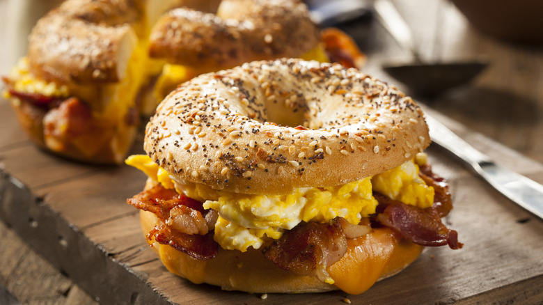 Breakfast bagel with eggs and bacon on a wooden cutting board