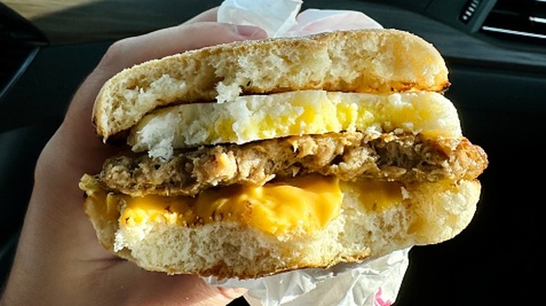 Hand holding bitten breakfast sandwich with egg, patty, cheese