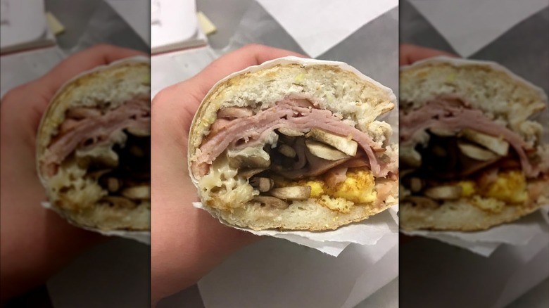 Hand holds a Potbelly breakfast sandwich with ham, mushrooms, and eggs