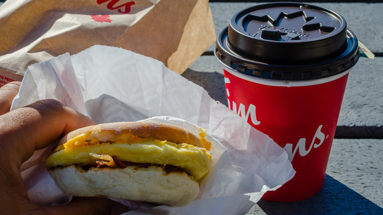 Hand holding Tim Hortons breakfast sandwich with coffee cup