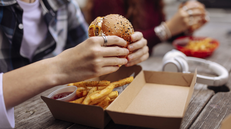 Person eating fast food burgers and fries from a to-go box.