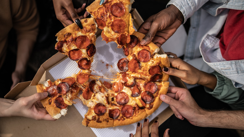 Hands pulling pepperoni pizza