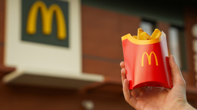 Hand holding up a container of McDonald's fries in front of restaurant