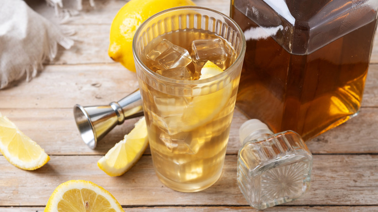 Highball cocktail displayed with a bottle of whisky and lemons on a wooden surface.
