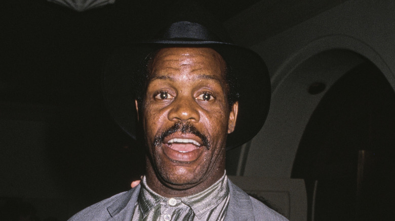 1980s superstar Danny Glover wearing a gray shirt and black hat