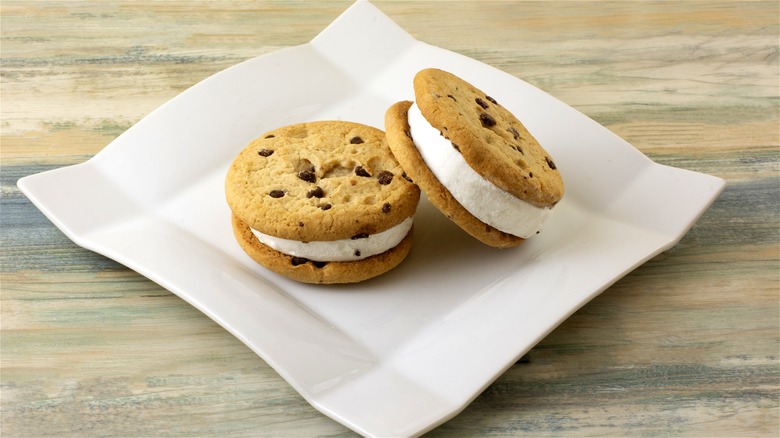 Ice cream sandwiches made with chocolate chip cookies and vanilla ice cream on a white plate.