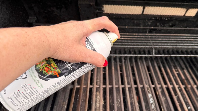 Hand holding bottle of cooking spray over grill