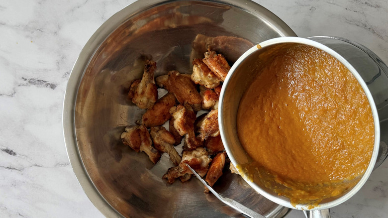 Sauce from pan pouring into bowl of chicken wings