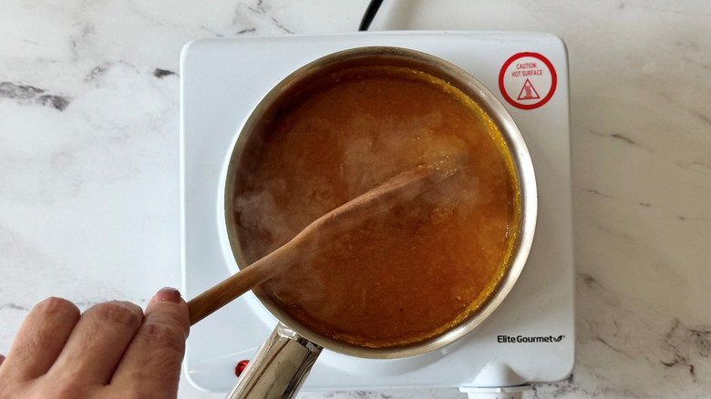 Stirring mango habanero sauce in saucepan with wooden spoon