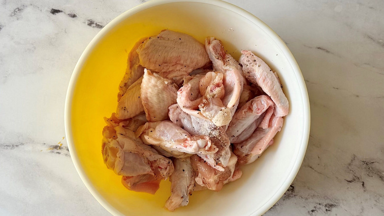 Raw chicken wings seasoned with salt and pepper in bowl