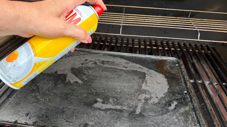 Hand spraying griddle with cooking spray