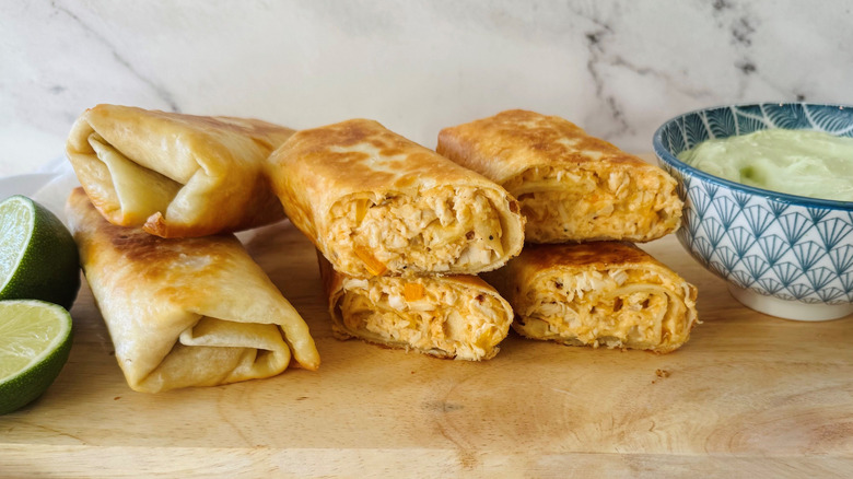 Chicken wraps stacked on wooden board next to avocado lime dip