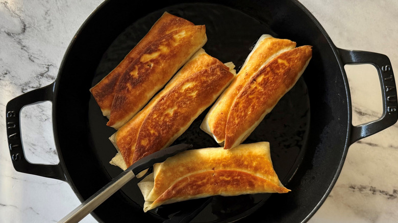 Tongs flipping tortilla wraps in skillet