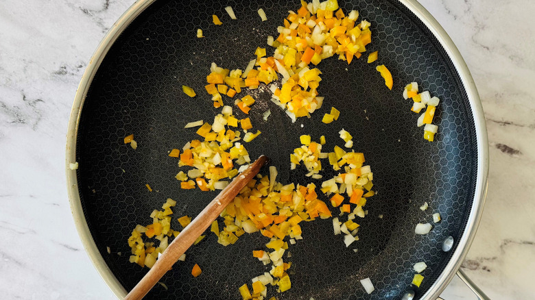 Wooden spoon stirring diced aromatics in pan