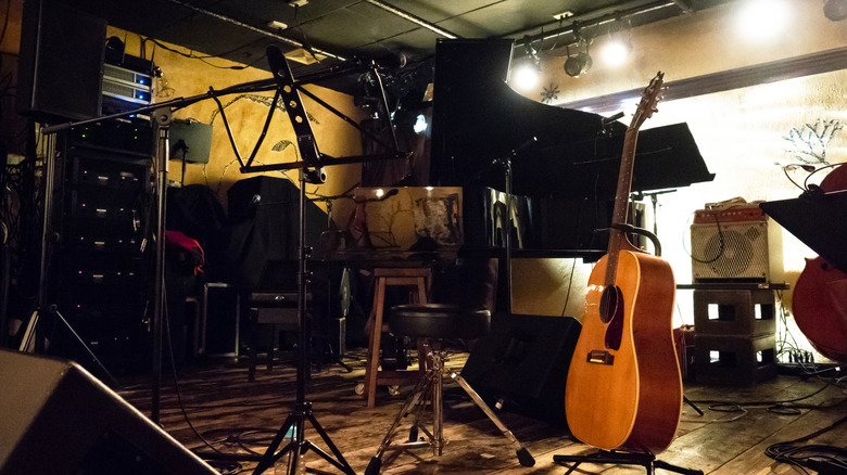 An empty stage with an acoustic guitar on a stand.