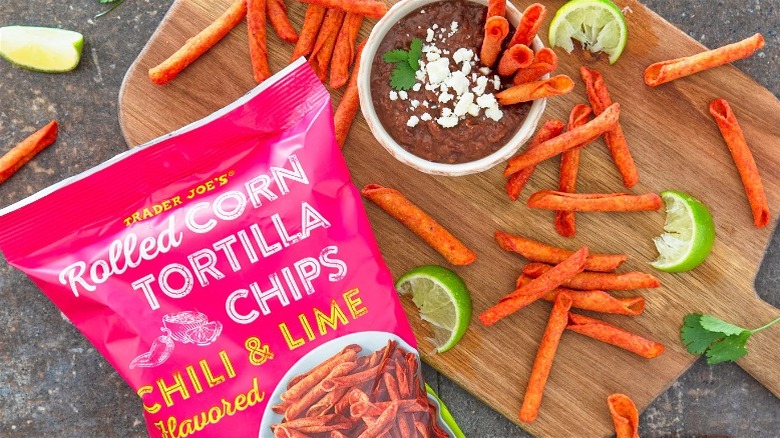 Trader Joe's chili and lime-flavored rolled corn tortilla chips with bean dip on wooden cutting board.