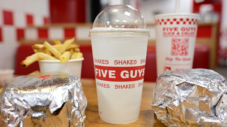 A meal with two foil-wrapped sandwiches, fries, and two drinks from Five Guys