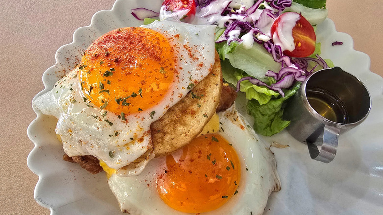 Basted, sunny-side-up eggs topped with herbs and spices on plate with a salad and olive oil on the side.