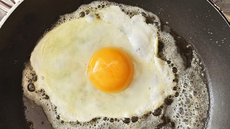 A sunny-side-up egg frying in a pan with butter.