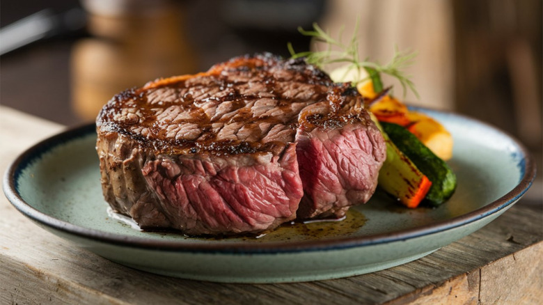 Steak on plate with vegetables atop wooden table.
