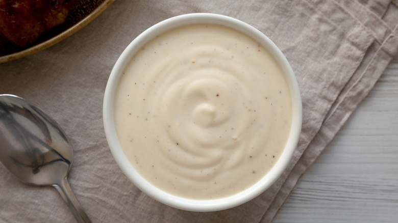 A bowl of white sauce with black flecks sits on top a napkin. A spoon and another bowl sit to its left.