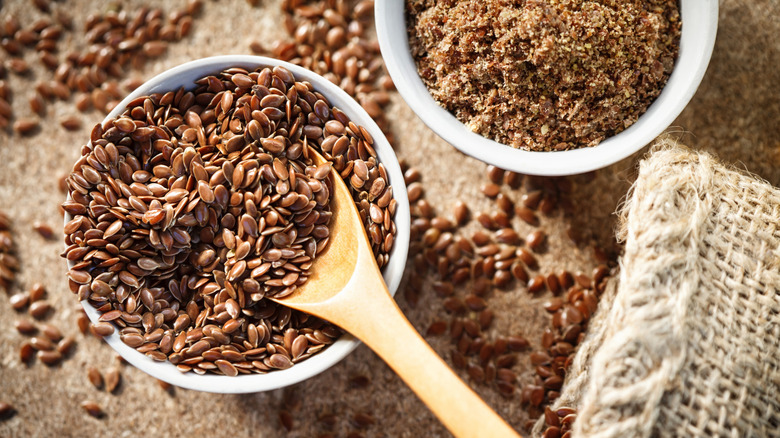 Flax seeds in a bowl beside a bowl of ground flax seeds and a burlap bag