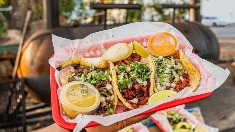 Holding tacos from Taqueria El Asador with smoker in the background