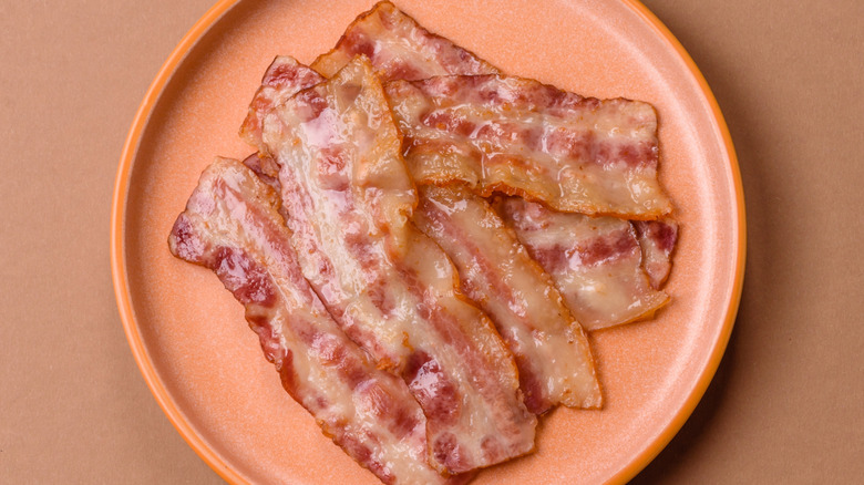 Pinkish plate of fairly straight bacon slices with grease on tan background