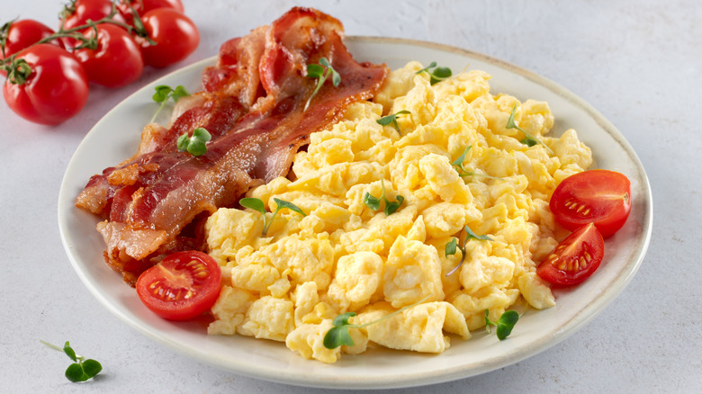 A plate of scrambled eggs, bacon, and tomatoes.
