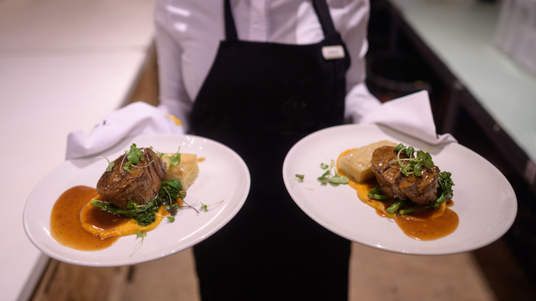A waiter holding two hot plates with grilled steak