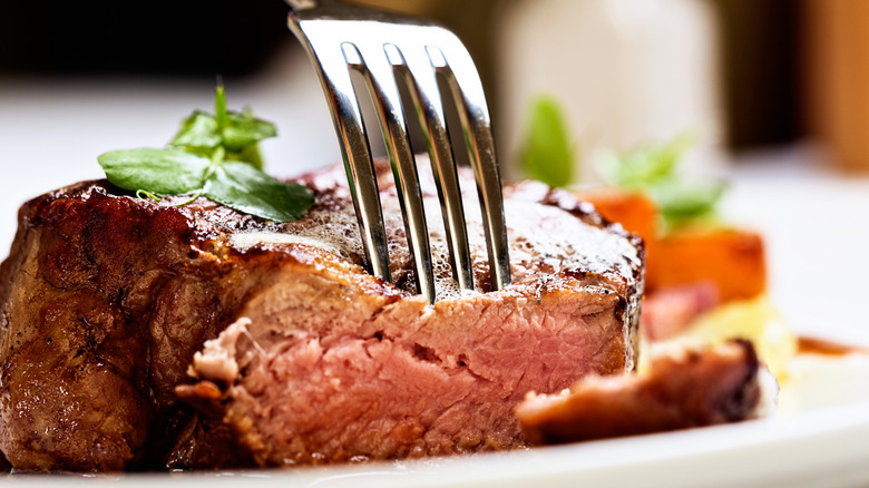 A fork piercing a grilled filet steak