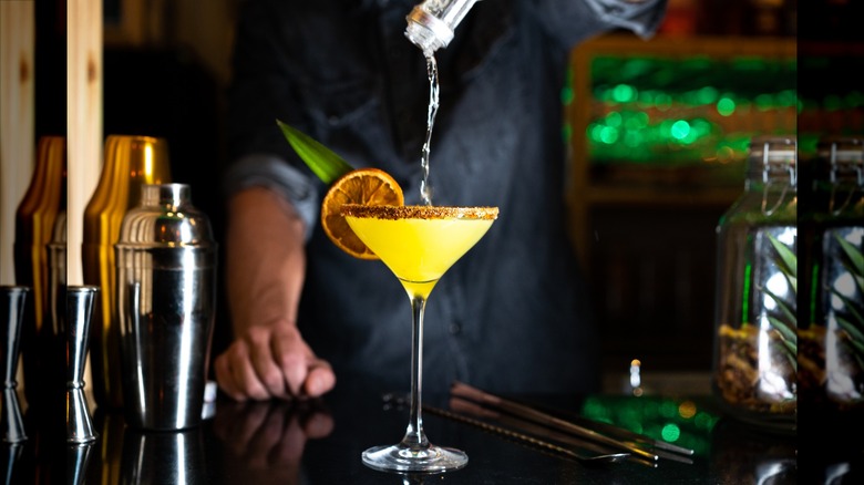 bartender pouring cocktail into a martini glass with orange garnish