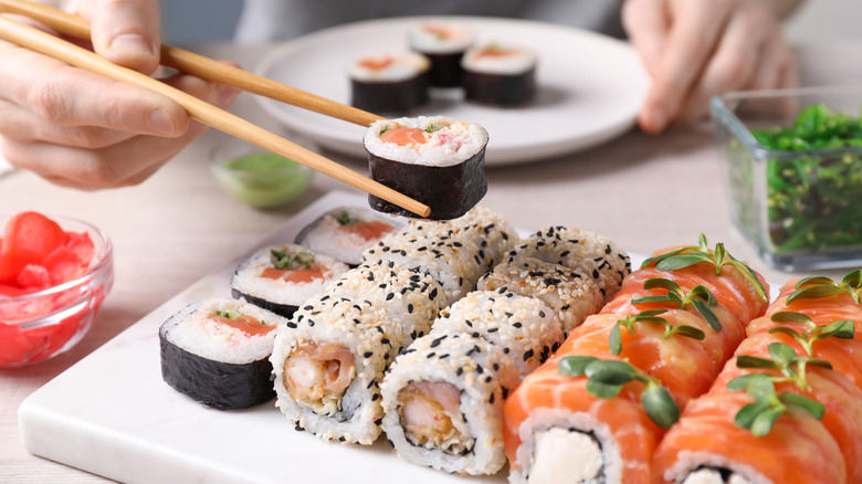 A plate of various types of sushi rolls and one being picked up with chopsticks