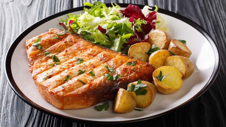 Swordfish steak on plate with green salad and roasted potatoes.