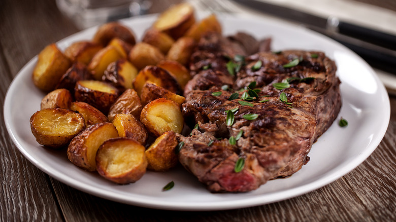 Grilled steak with roasted potatoes on white plate.