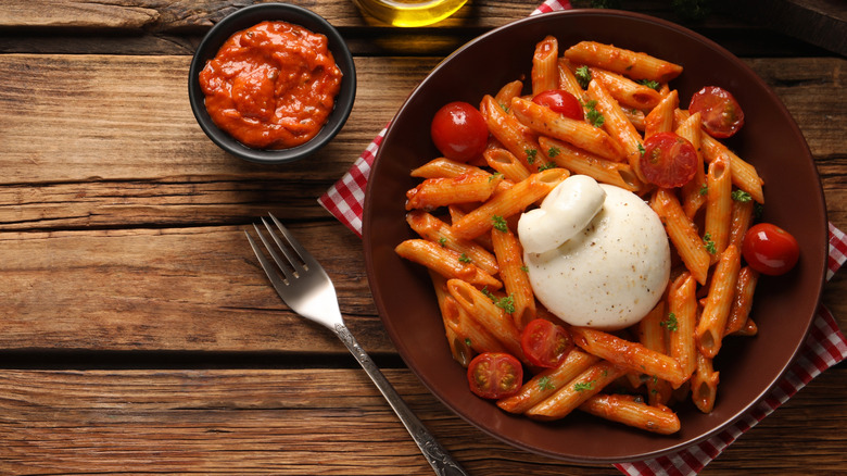 A bowl of penne pasta with tomato sauce and cherry tomatoes on a wooden table