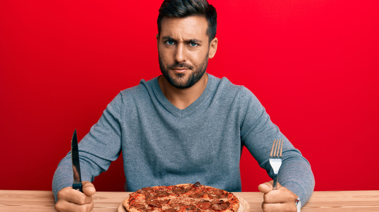 Man eating pizza with a fork and knife. 